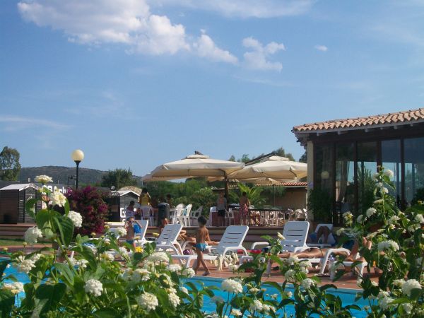 Piscina con sedie a sdraio, persone che si rilassano e ombrelloni beige.