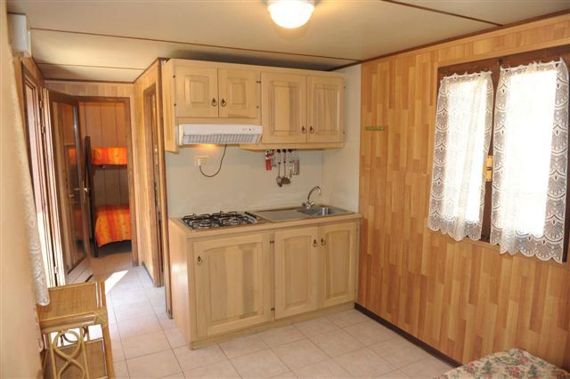 Cucina in legno chiaro con fornello, lavello e armadietti, luce naturale.