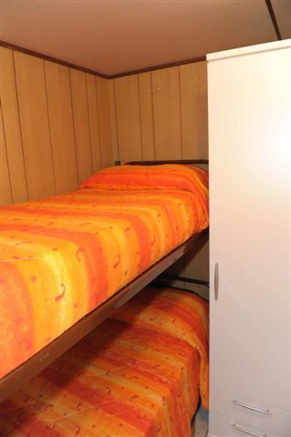 Letto a castello con coperte arancioni e bianco in una stanza con armadio bianco.