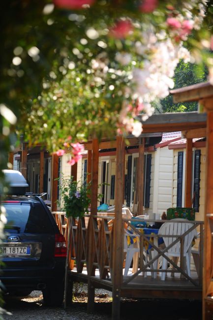 Una fila di case mobili con veranda e un'auto parcheggiata, circondate da vegetazione e fiori.