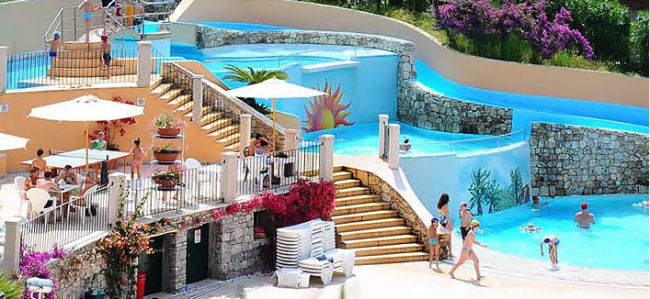 Piscina con scivoli, sedie a sdraio e persone che relax.