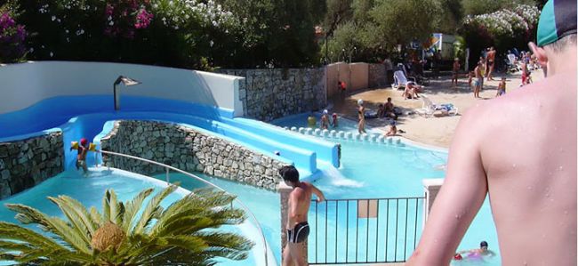 Un parco acquatico con scivoli d'acqua, piscine e visitatori che si divertono sotto il sole.