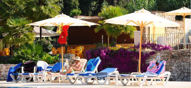Lettini e ombrelloni bianchi vicino a una piscina, circondati da piante e fiori.