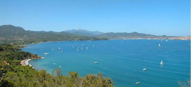 Vista panoramica di una baia con vele bianche e colline sullo sfondo.