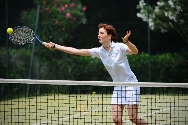 Una donna in divisa bianca colpisce una palla da tennis su un campo.