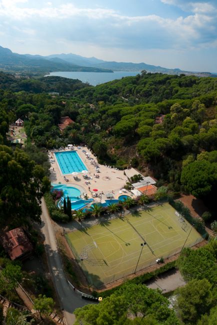 Veduta aerea di piscine, campi da tennis e vegetazione rigogliosa vicino al mare.