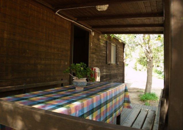 Tavolo con tovaglia a quadri su veranda di legno accanto a una casetta.