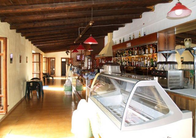 Un interno di bar con soffitto in legno, bancone con alcolici e una vetrina per gelato.