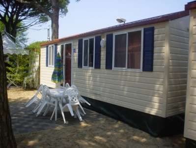 Casa mobile chiara con finestre blu, tavolo e sedie bianche all'esterno.