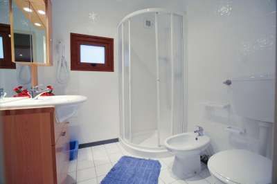 Bagno con doccia circolare, lavandino e WC bianchi.