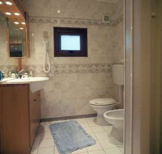 Bagno con lavabo, specchio, wc e finestra piccola, pavimento piastrellato.
