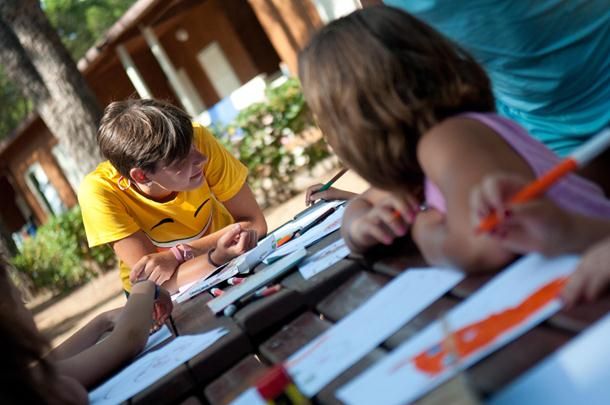 Bambini e un adulto seduti attorno a un tavolo all'aperto mentre disegnano.