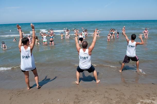 Tre istruttori sulla spiaggia guidano un gruppo di persone in acqua.