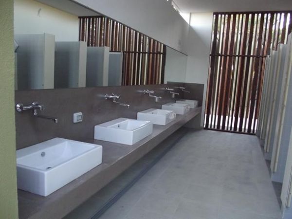 Bagno pubblico elegante con lavandini in fila e divisori.