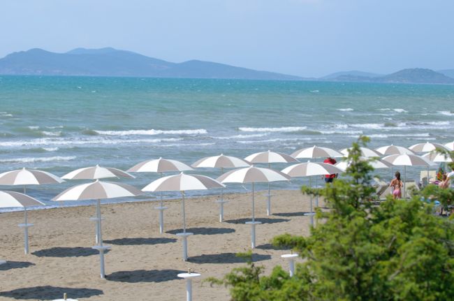 Una spiaggia sabbiosa con ombrelloni bianchi e il mare sullo sfondo.