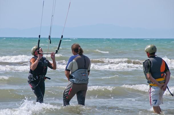 Persone fanno kitesurf in mare, con attrezzatura e caschi protettivi.