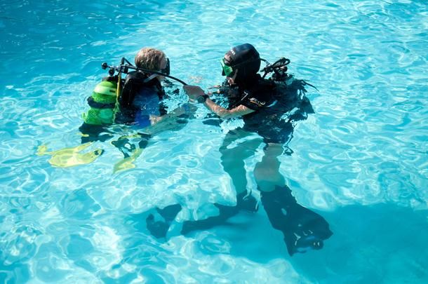 Due subacquei in piscina, in tenuta completa con bombole e maschere.