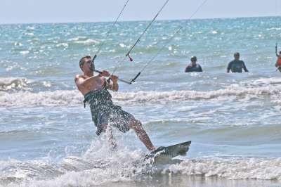Un uomo pratica kitesurf sulle onde, tenendo saldamente la barra del kite.