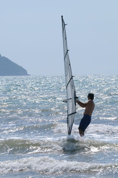 Una persona fa windsurf tra le onde di fronte a un paesaggio collinare.