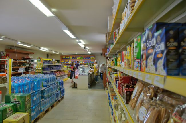 Interno di supermercato con file di prodotti alimentari e acqua.