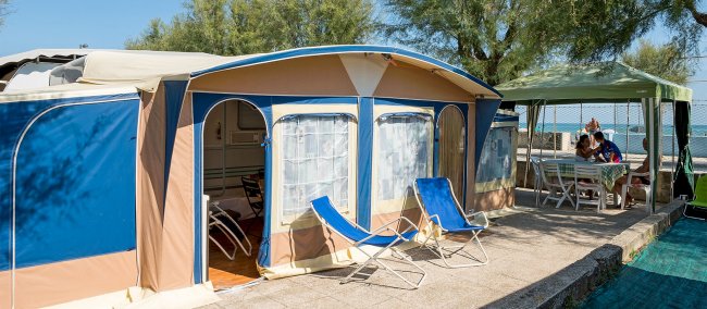Camper con veranda e lettini su un piazzale vicino al mare.