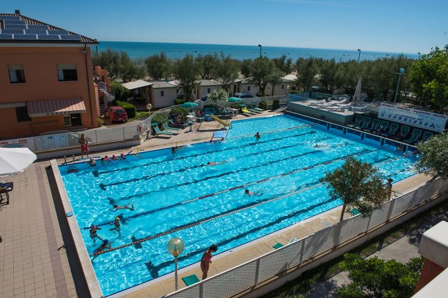 Piscina all'aperto con nuotatori e vista mare.