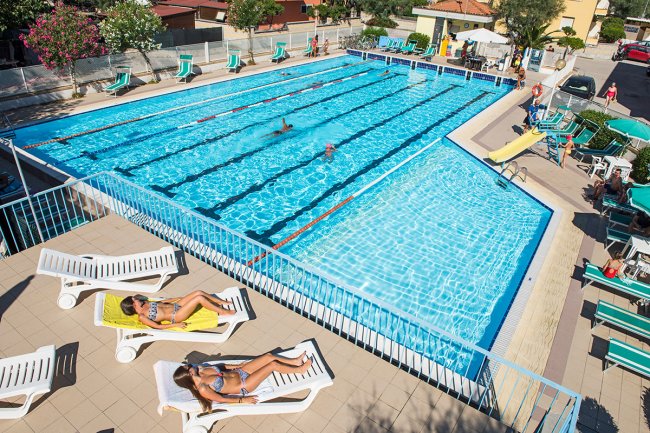 Piscina con sdraio e persone che prendono il sole.