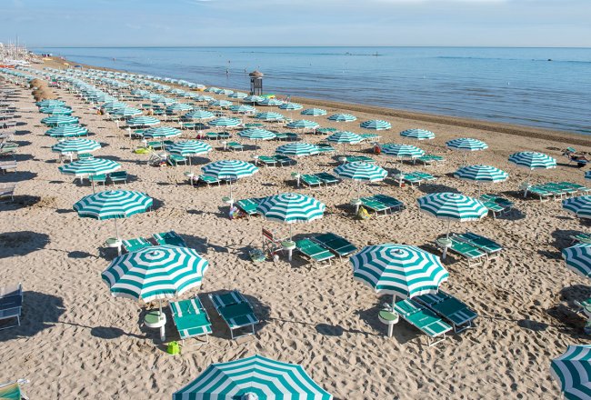 Spiaggia con ombrelloni a strisce verde e bianco.