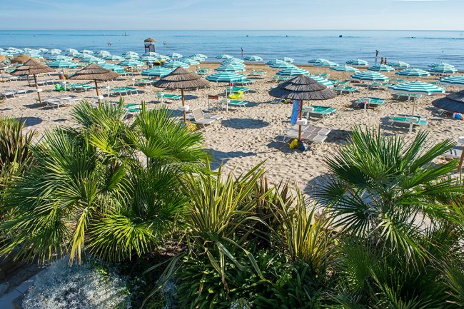 Spiaggia con ombrelloni a strisce e piante tropicali.