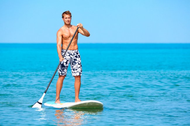 Uomo in piedi su una tavola da paddle in mare.