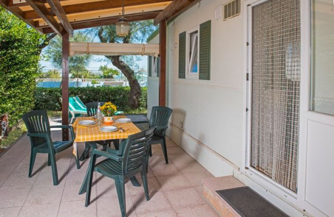 Veranda con tavolo apparecchiato e sedie verdi.