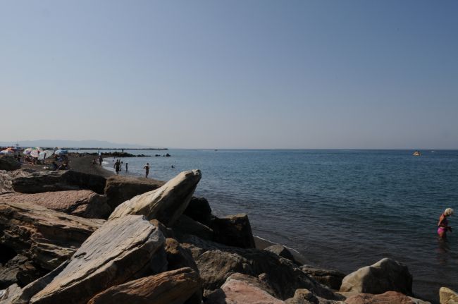 Spiaggia rocciosa con bagnanti e mare calmo sotto un cielo limpido.