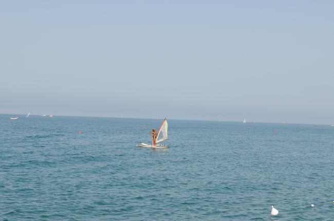 Una persona fa windsurf su un mare calmo sotto un cielo sereno.