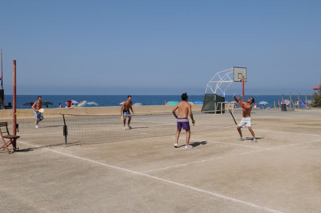 Quattro uomini giocano a pallavolo su un campo all'aperto vicino alla spiaggia.