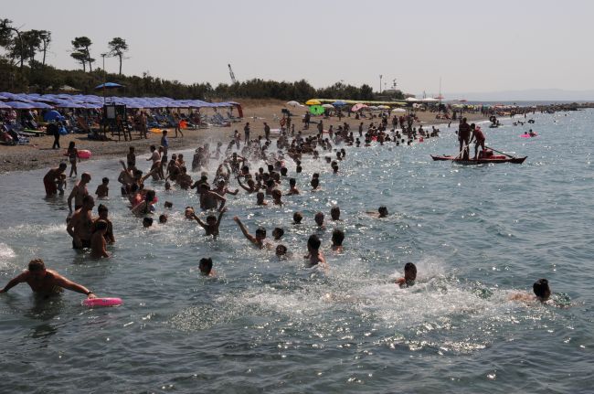 Spiaggia affollata con persone che nuotano nel mare e ombrelloni colorati sulla sabbia.