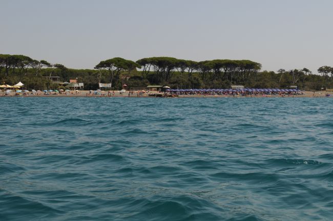 Spiaggia affollata con ombrelloni blu vista dal mare.