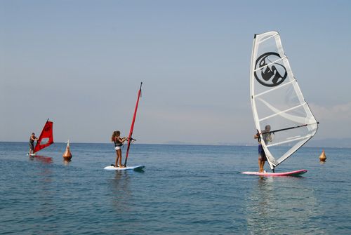 Tre persone praticano windsurf su un mare calmo con vele colorate.