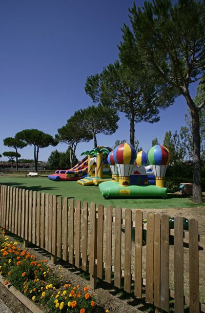 Un'area giochi all'aperto con gonfiabili colorati, alberi e una recinzione in legno.