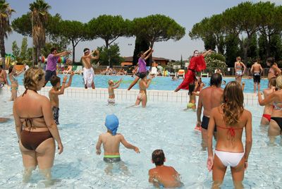 Persone in costume fanno attività in una piscina all'aperto con alberi intorno.