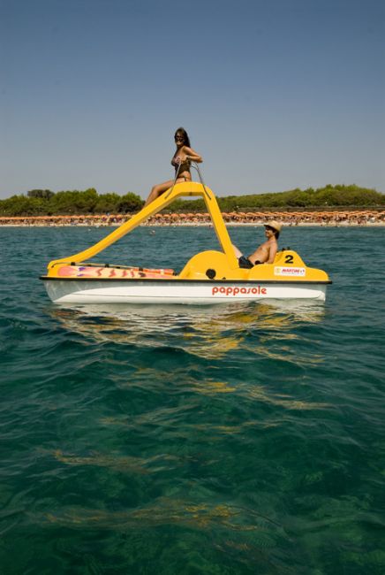 Due persone su un pedalò giallo in mare con costa verde sullo sfondo.