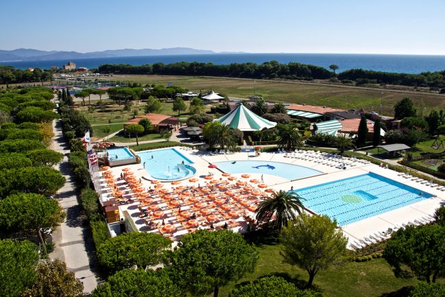 Vista piscina con ombrelloni arancioni, giardino verde e mare sullo sfondo.