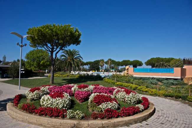 Giardino con aiuola di fiori rossi e bianchi, alberi e sentiero curvo.