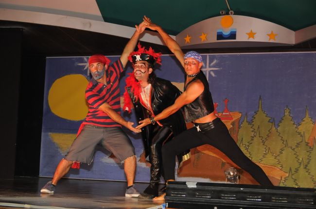 Tre attori in costume su un palco, con sfondo dipinto di paesaggio.