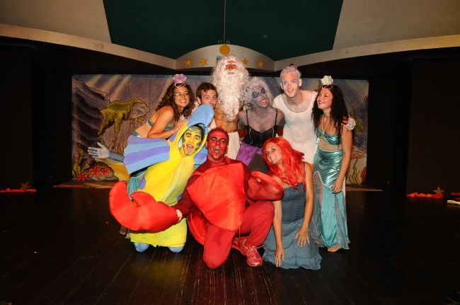 Persone in costume recitano una scena teatrale con tema sirene e creature marine.