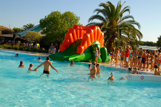 Una piscina all'aperto con uno scivolo gonfiabile arancione e verde, circondata da palme.