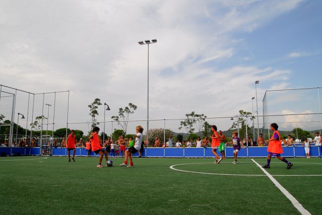 Bambini che giocano a calcio su un campo recintato, indossando pettorine rosse.
