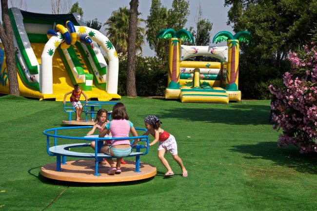 Bambini giocano su una giostra e scivoli gonfiabili in un parco giochi.