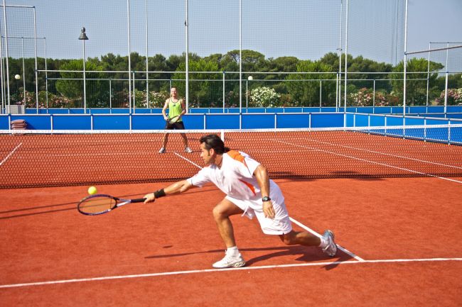 Due persone giocano a tennis su un campo all'aperto in terra rossa.