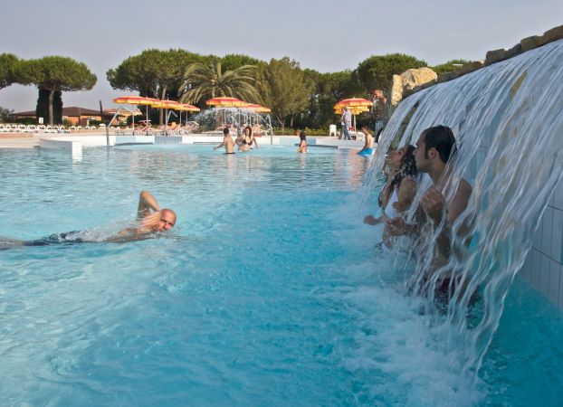 Una piscina con una cascata d'acqua e persone nuotando e giocando.