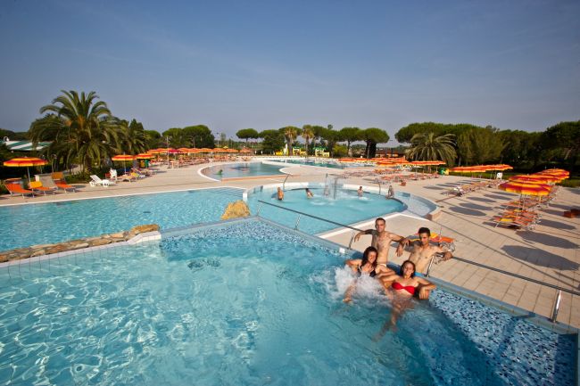 Un gruppo di quattro persone si diverte in una piscina, circondata da ombrelloni e sdraio colorati.